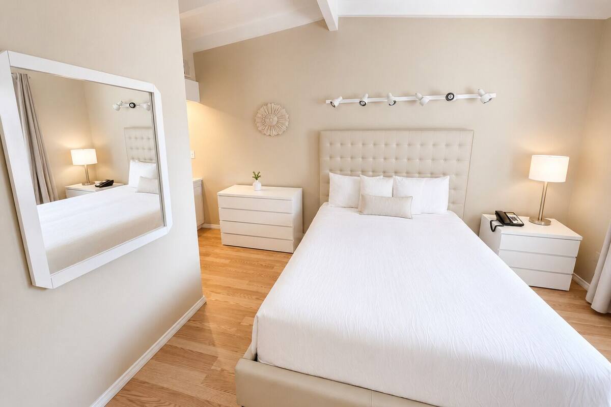Habitación de hotel con una cama grande, dos mesitas de noche, un espejo y una lámpara fijada a la pared.