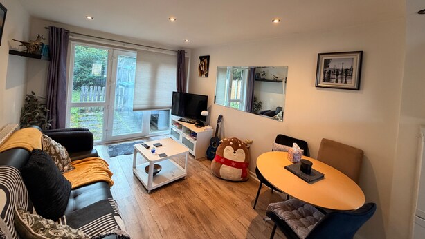 A living room with a sofa, a coffee table, a TV, a dining table, and a window with curtains.