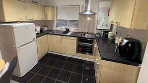 A compact kitchen with a refrigerator, stove, sink, and a window with blinds.