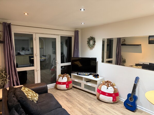 Una sala de estar con un sofá, dos sillones de peluche, un televisor y una guitarra.