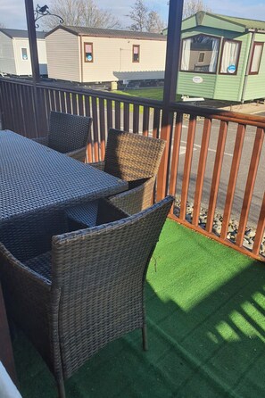 A balcony with wicker furniture, a green artificial turf, and a view of mobile homes. - Wooden Lodge, Sleeps 9 with Veranda & Decking (Fleetwood)