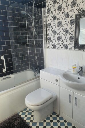 A bathroom with a bathtub, toilet, and sink, featuring black and white patterned tiles and a checkered floor. - Wooden Lodge, Sleeps 9 with Veranda & Decking (Fleetwood)