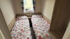 A small room with two single beds, a window with curtains, and a wooden floor. - Seaside Caravan Sleeps 7 - Pet Friendly, Garden (Rhyl)