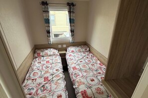 A small room with two single beds, a window with curtains, and a wooden floor. - Seaside Caravan Sleeps 7 - Pet Friendly, Garden (Rhyl)