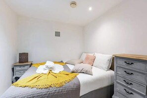 A bedroom with a bed, a nightstand, a dresser, and a wall-mounted light fixture. - Earls Court Apt, Sleeps 3 with Private Entrance (London)