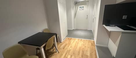 A room with a wooden floor, a black table with two chairs, a television on a stand, and a door leading to another room.