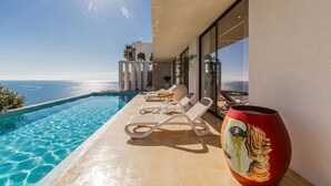 Zona junto a la piscina con sillas de descanso y un florero decorativo.