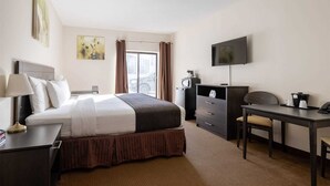 A hotel room with a bed, desk, chair, TV, and a window with curtains.