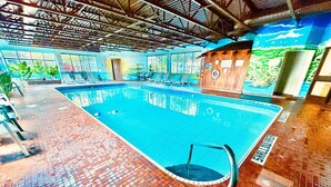 An indoor swimming pool with tiled flooring, a diving board, and a wooden cabin-like structure.