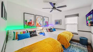 Habitación de hotel con dos camas, ventilador de techo, obras de arte enmarcadas en la pared y ventana con persianas.