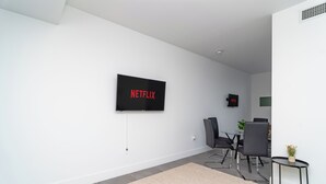 A modern living room with a flat-screen TV mounted on the wall, a dining table with chairs, and a small side table with a plant. - Central 1BR in Miami Near Wynwood and Marlins Park (Miami)