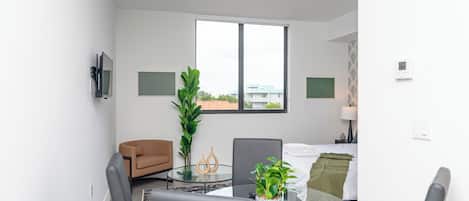 Uma sala de estar moderna com uma mesa de vidro, duas cadeiras, um sofá, uma janela grande e um vaso de plantas.