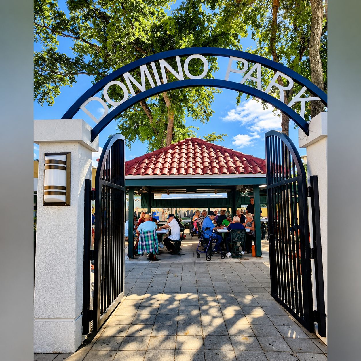 Une entrée fermée par un portail donnant sur le parc Domino, avec une structure surmontée d’un toit en tuiles et des personnes rassemblées à l’intérieur.