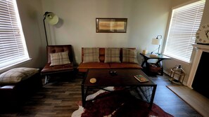 Ein Wohnzimmer mit einer Couch, Sesseln, einem Couchtisch, einem gerahmten Bild an der Wand und einer Wanduhr.