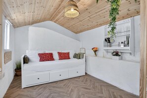 Ett rum med en vit soffa, en hängande växt, ett träpanelat tak och en vit vägg med en hylla.