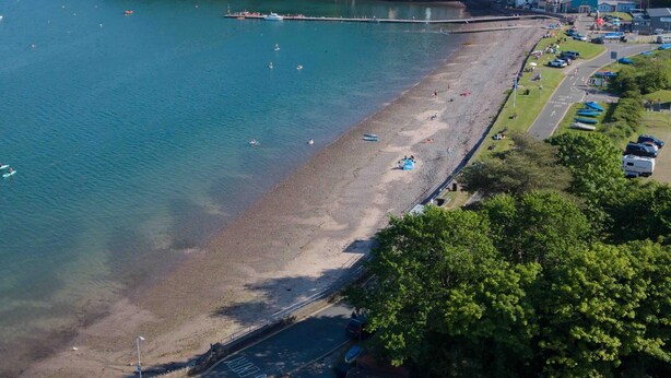 Una zona costera con playa, muelle y una carretera que conduce a un pequeño edificio.