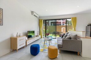 A modern living room with a sofa, ottoman, TV, and a dining area with yellow curtains.