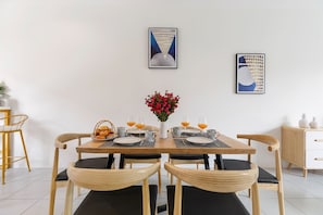 A dining area with a wooden table, four chairs, a vase of flowers, and two framed artworks on the wall.