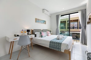 A modern hotel room with a bed, desk, chair, and a balcony with a view.