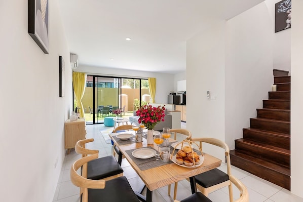 A dining area with a wooden table, chairs, and a breakfast setting including flowers, orange juice, and pastries.