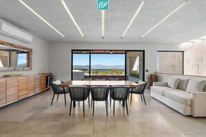 Ein modernes Interieur mit Essbereich, einer Couch und einem großen Fenster mit Meerblick.