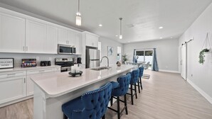 Una cocina moderna con armarios blancos, electrodomésticos de acero inoxidable y una zona de bar con taburetes azules.
