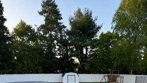 Un jardin avec un trampoline, une aire de jeux, un abri de jardin et une clôture blanche.