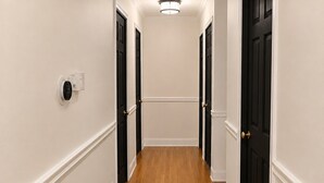 Un couloir avec un plancher en bois, des murs blancs et des portes noires.