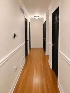 A hallway with wooden flooring, white walls, and black doors.