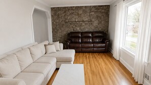 Un salon spacieux avec un canapé d’angle beige, une table basse blanche, un canapé en cuir et un mur en pierre.