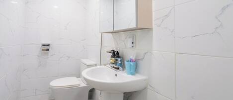 A bathroom with a toilet, sink, mirror, and a trash bin.