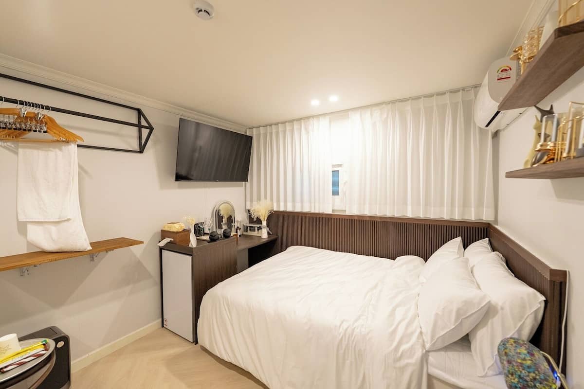 Quarto de hotel com cama, escrivaninha com espelho, televisão na parede e janela com cortinas.