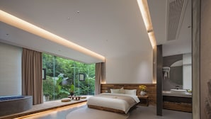 Un dormitorio moderno con una cama grande, un ventanal integrado y un pequeño rincón de descanso.
