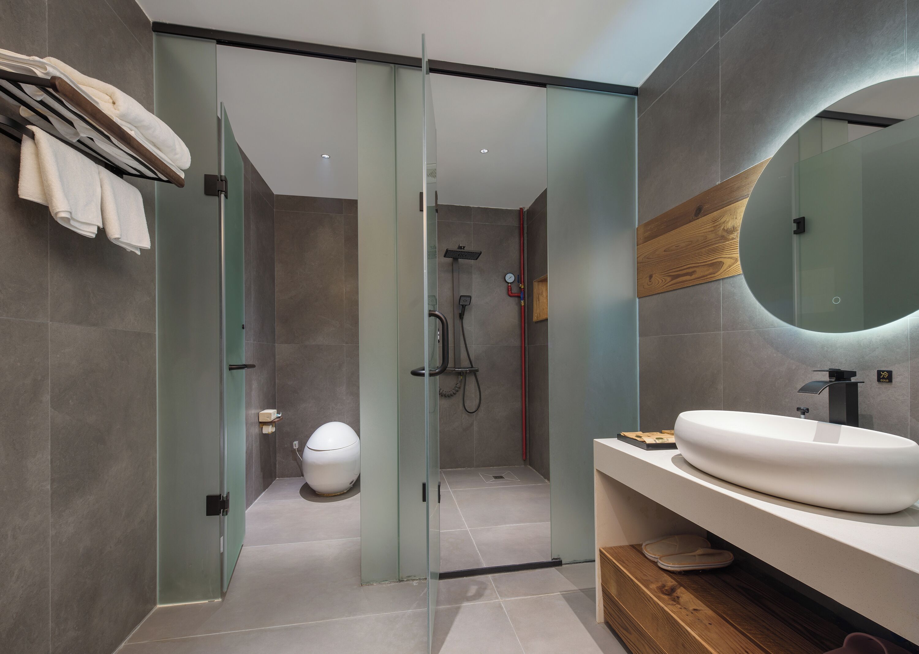 Un baño moderno con ducha envuelta en vidrio, un lavamanos blanco y un mueble de tocador de madera.