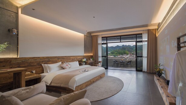 Una habitación de hotel moderna con una cama grande, un área de descanso con una mesa y un balcón con vistas a la ciudad.