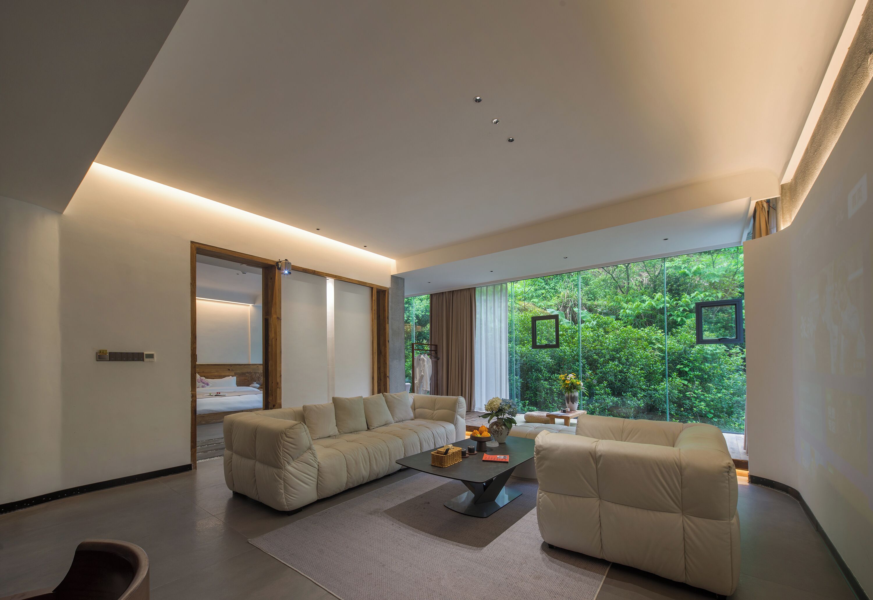 A modern living room with a sectional sofa, a coffee table, and a large window offering a view of greenery.