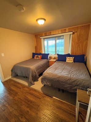 A bedroom with two beds, wooden paneling, a window with a view, and a ceiling light.