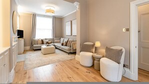 A living room with a sofa, ottoman, armchair, and a small table with a lamp. - 5-bed Chelsea Home Next To Kings Road (London)