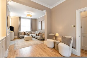 Ein Wohnzimmer mit Sofa, Hocker, Sesseln und einem kleinen Tisch mit Lampe.