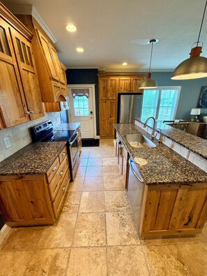 A kitchen with wooden cabinets, granite countertops, a stainless steel refrigerator, and pendant lighting. - Historic Charm, Modern Comfort Close to Downtown with AC Family and Pet Friendly (Dickinson)