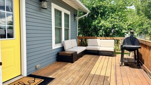 Una terraza con un banco de madera, una parrilla y una puerta amarilla.