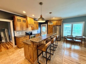 A kitchen with wooden cabinets, a granite countertop, a stainless steel refrigerator, and a bar area with stools. - Historic Charm, Modern Comfort Close to Downtown with AC Family and Pet Friendly (Dickinson)