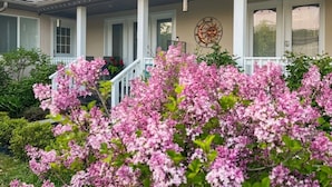 Une maison avec un porche, une décoration murale représentant le soleil et la lune, et des fleurs roses en pleine floraison.