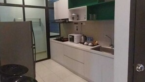 A compact kitchen with white cabinets, a microwave, a sink, and a green shelf. - Sekata Apartment (Ringlet)