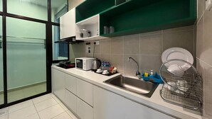A modern kitchen with a microwave, kettle, and sink. There are green shelves above the counter and a window with frosted glass. - Sekata Apartment (Ringlet)