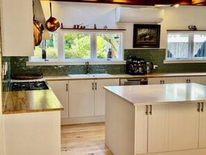 A modern kitchen with a gas stove, white cabinets, a coffee machine, and a view of greenery outside.
