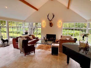 A spacious living room with a fireplace, leather sofas, a glass coffee table, and a grand piano.