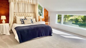 Une chambre à coucher avec une tête de lit capitonnée, un lit à baldaquin, une grande fenêtre et un lustre.