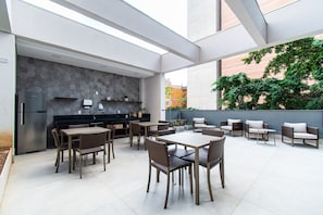 A modern outdoor dining area with a kitchen, seating, and a view of the city. - Pause Living - Nex One Paraíso (São Paulo)