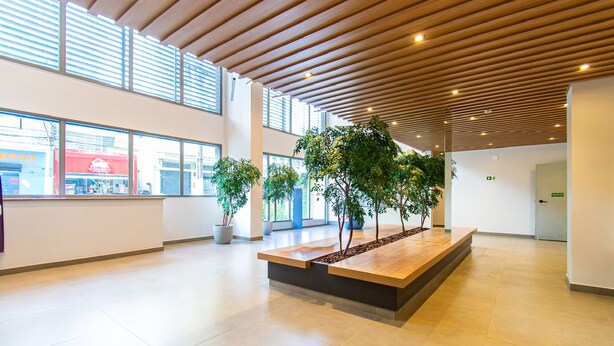 A spacious lobby with a wooden ceiling, large windows, and potted plants. - Pause Living - Nex One Paraíso (São Paulo)
